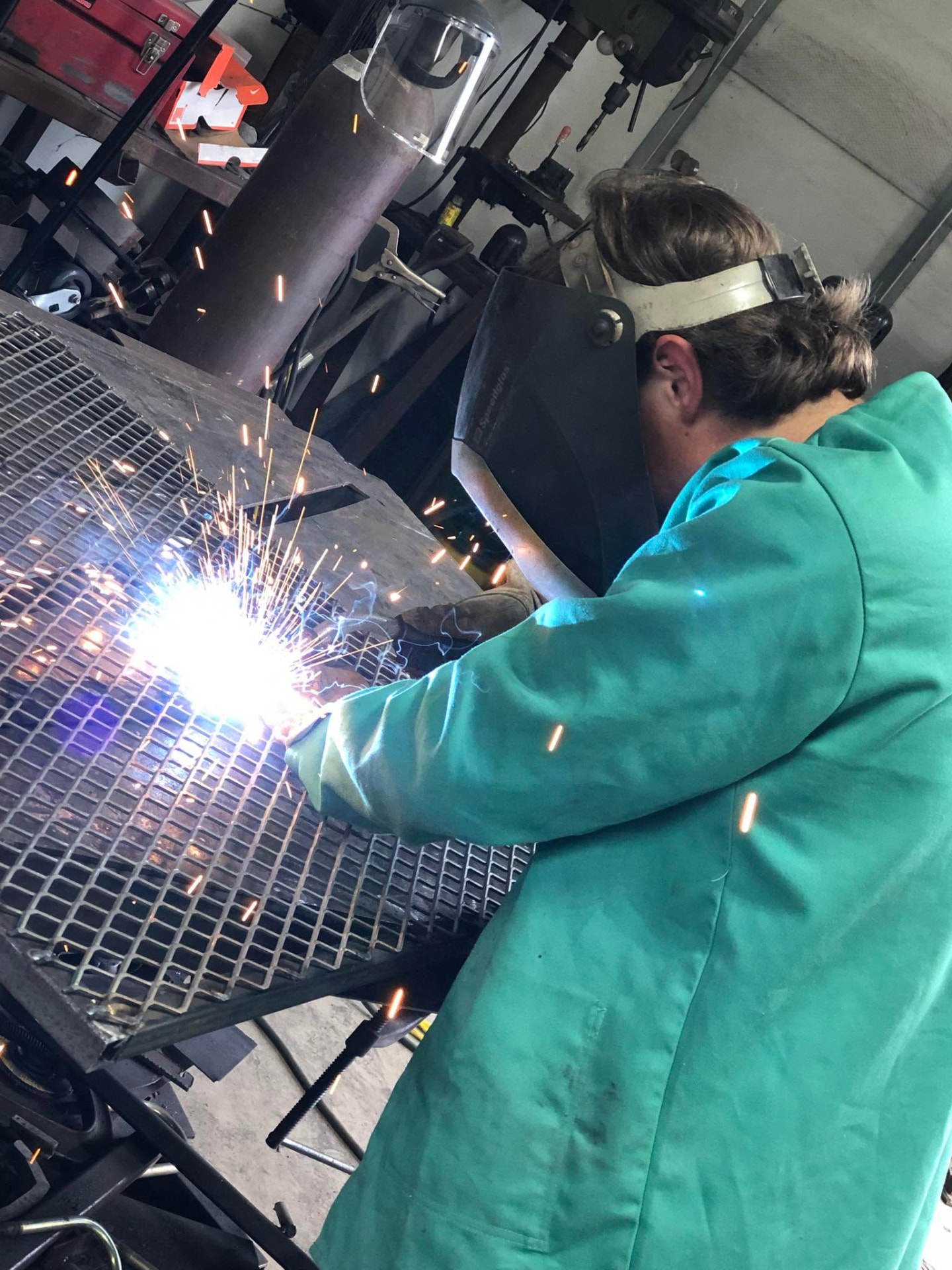 Welder laying a bead on a steel grate table with bright sparks